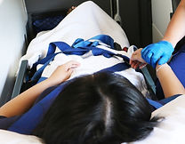 Imagem interna de uma ambulância de cuidados básicos, com uma paciente deitada na maca e a técnica em enfermagem segurando sua mão.