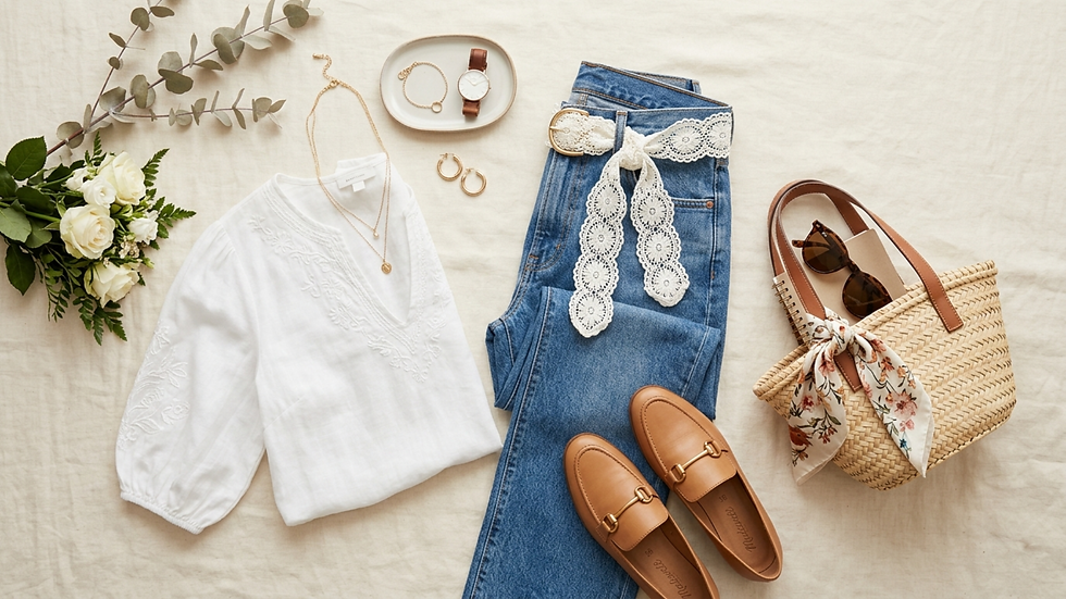 Flat lay de moda: blusa blanca bordada, jeans con encaje, mocasines, bolso de rafia y accesorios sobre fondo beige.