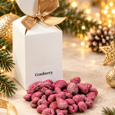 Rosa umhüllte Cranberrys neben einer weißen Geschenkverpackung mit goldener Schleife – fruchtig-süße Weihnachtsspezialität von It’s a Cake.