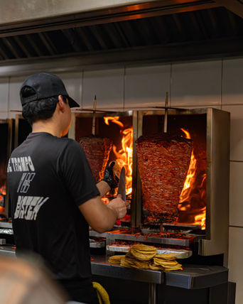 Taquero preparando un trompo de carne al pastor frente al fuego.
