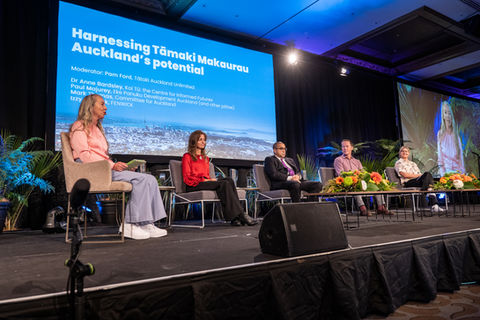 Four people are sitting on a stage in front of a large screen that says " harnessing tamaki makaurau "