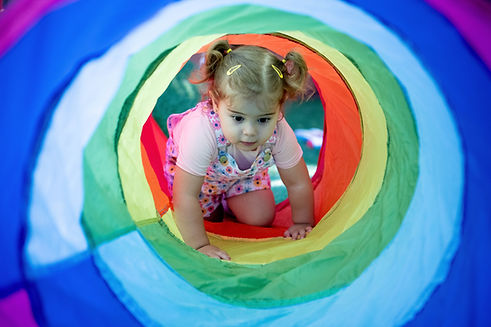 Toddler crawling through a colourful play tunnel at Bambini House childcare