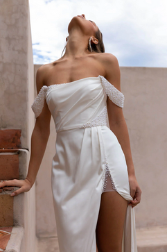 Bride wearing a white wedding dress with pearls and a leg slit looking up.