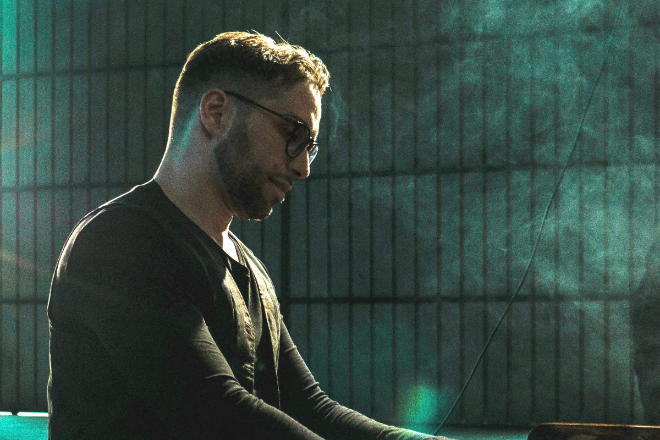 Antonio Simone, pianista jazz, ritratto di profilo mentre suona il pianoforte immerso in una luce soffusa con fumo di scena.