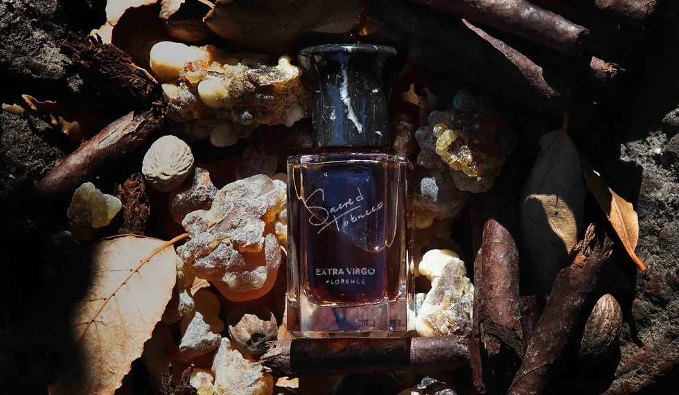 Flacone di Sacred Tobacco Extra Virgo tra fogliame di tabacco essiccato, legno e libri antichi