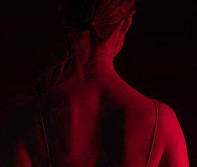 Woman's back and neck illuminated by red light, shoulder straps visible.