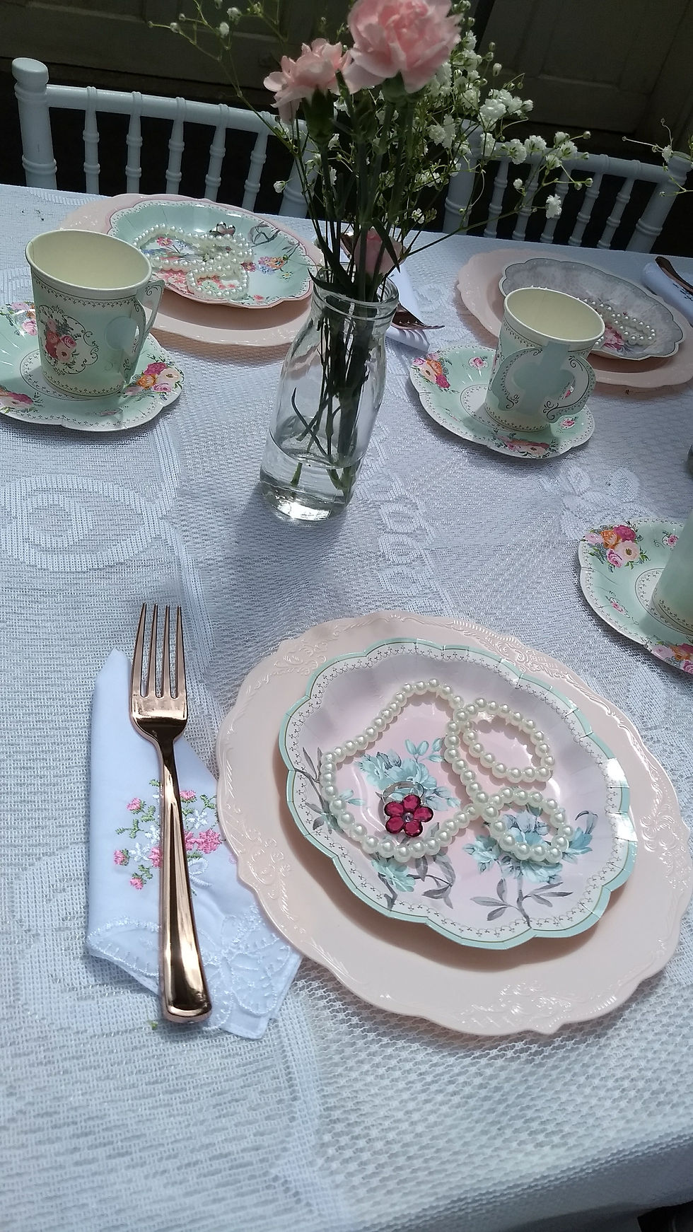 Vintage tea party table setting with paper cups and plates, mini milk bottle vases filled with carnations