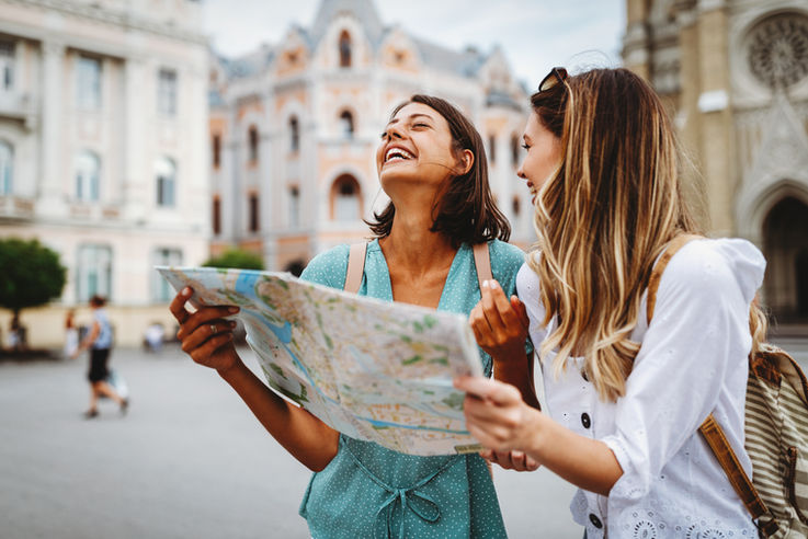 Zwei junge Frauen in einer Stadt halten eine Landkarte in der Hand und lachen. 