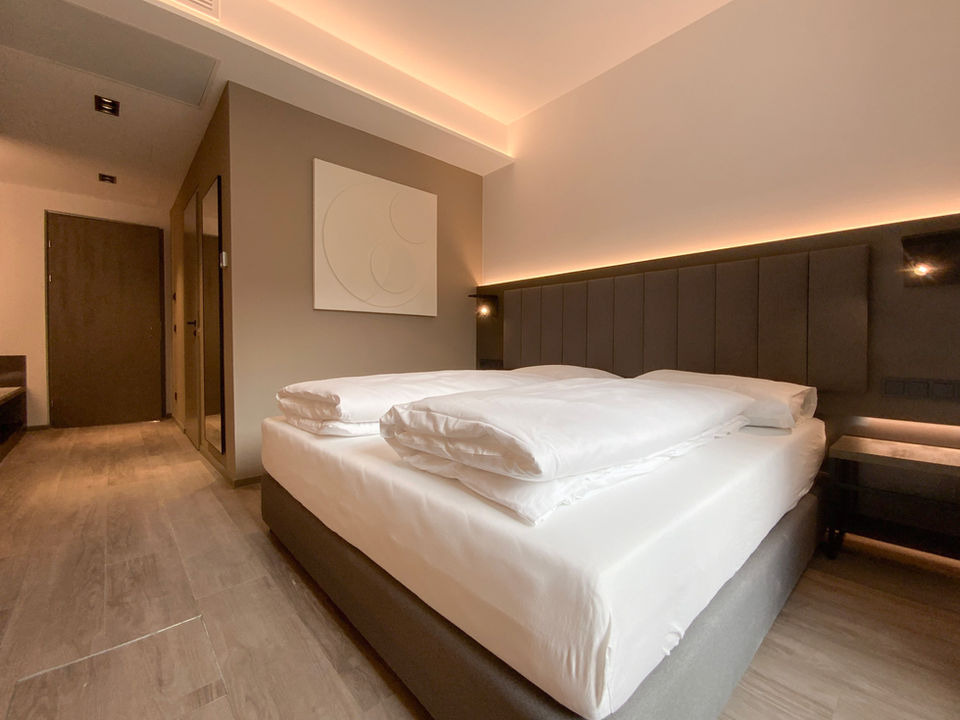Zimmerfoto des DION Hotel Wattens. Das Bett ist frisch bezogen. Das Zimmer ist in weiß, grau und braun gehalten.