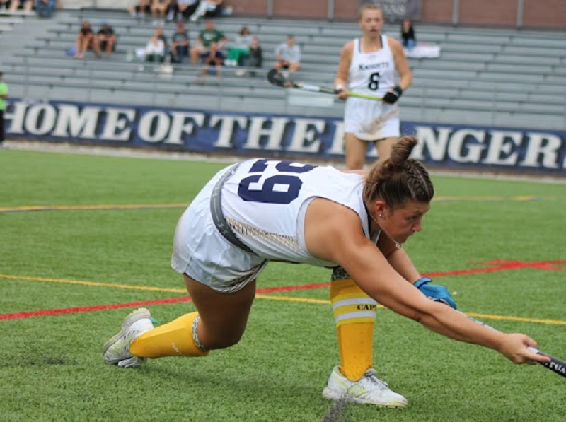 Field hockey athlete performing a low defensive reach on turf, demonstrating proper footwork, angles, and positioning to prevent attackers from getting past