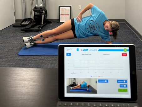 Athlete performing a side plank with motion sensors attached to legs while biomechanics software displays live movement data on a tablet.