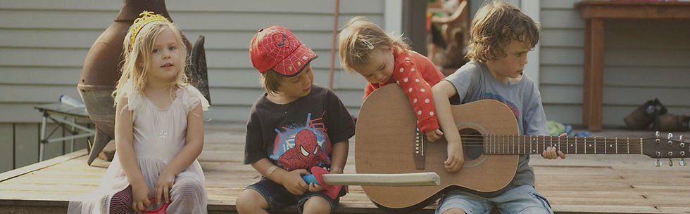 Four young children sitting outdoors, engaging with a guitar and playfully interacting, promoting awareness about auditory processing disorder in NZ