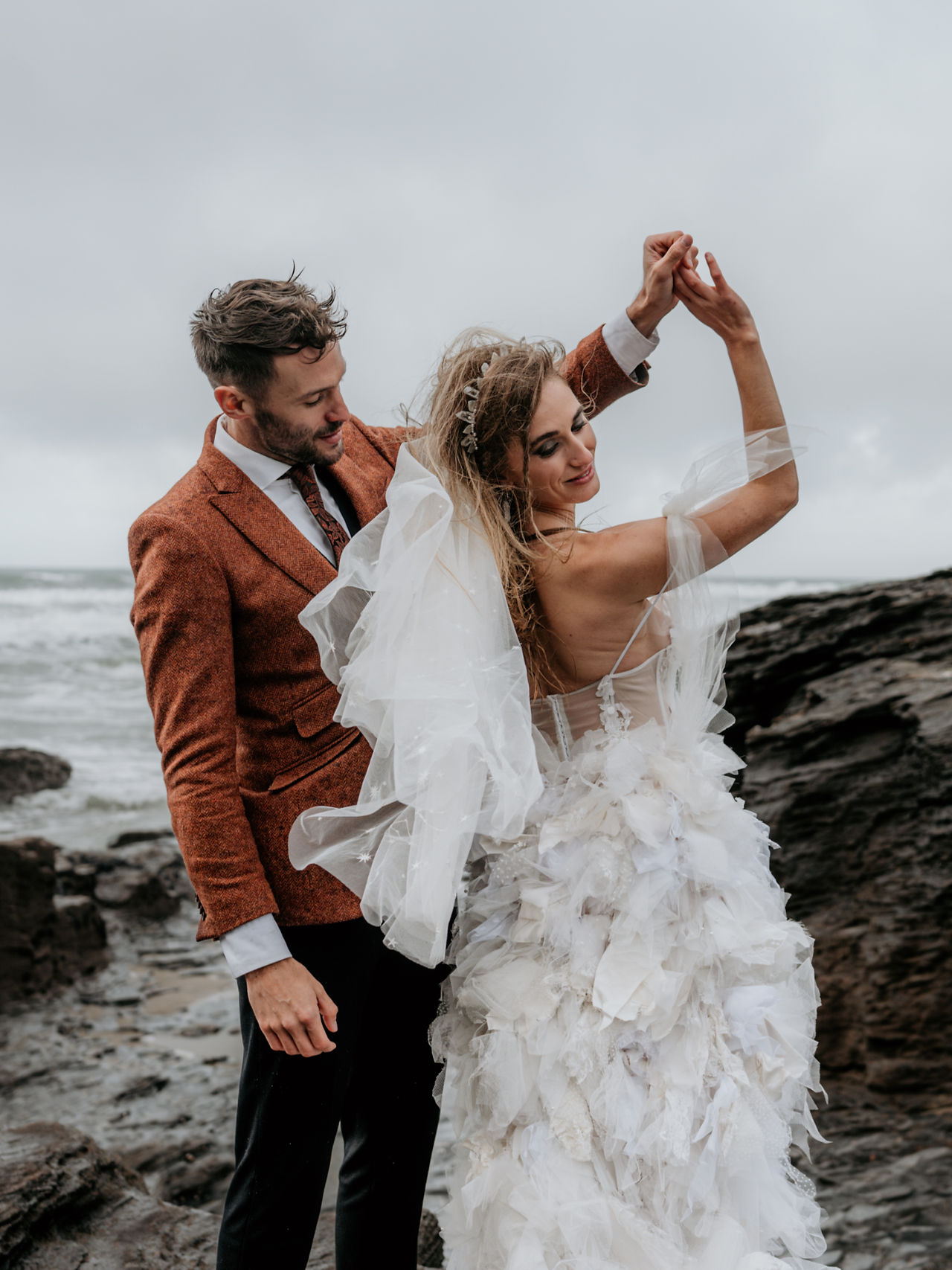 wild elopement couple on the beach. She wears a ruffled wedding dress with quartz and mother of pearl crown with a veil