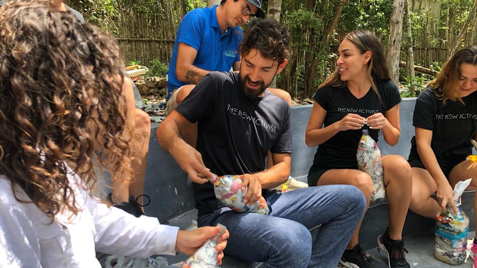 A group of people fills bottles with plastic waste outdoors. They wear "The New Activist" shirts. The mood is collaborative. Trees in background.