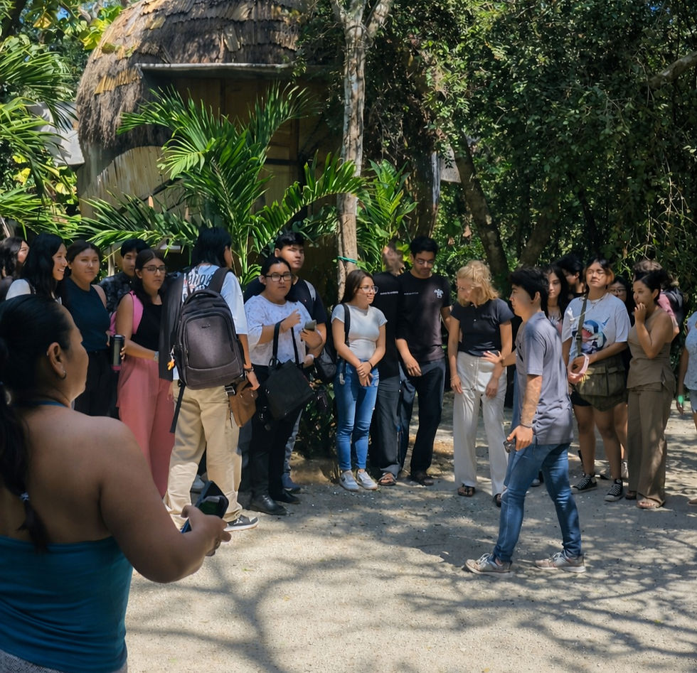 A group of people standing outdoors near a thatched-roof hut, surrounded by lush green foliage, in a sunny setting.