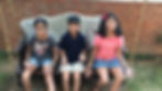 My kids proudly display their intricate henna designs while sitting on a swing, surrounded by a brick wall and a garden backdrop.