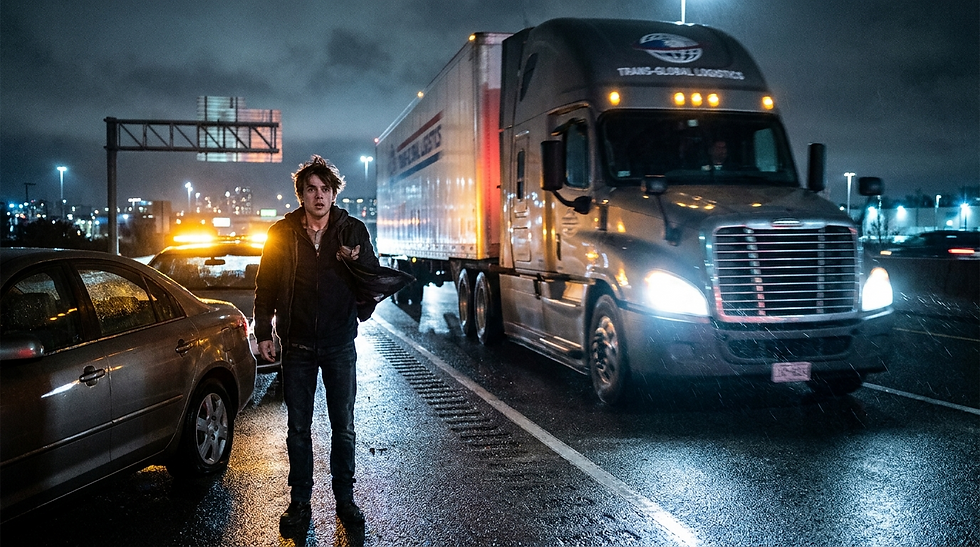 A man stranded on a highway at night with a truck approaching, illustrating the danger of roadside emergencies.