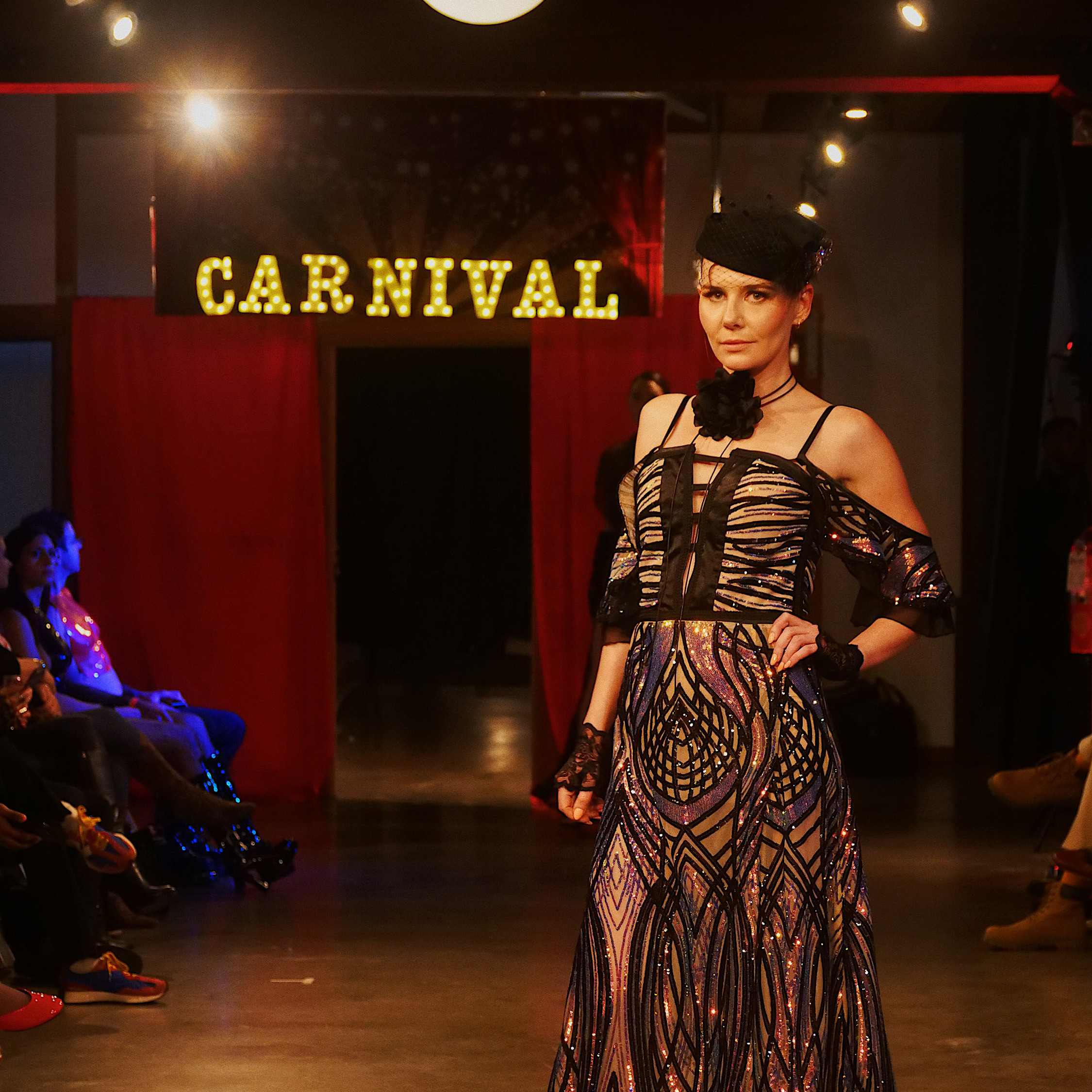 A model presenting a designer look on the Carnival runway, with guests watching