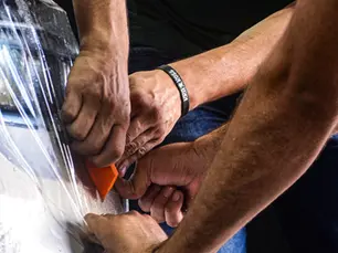 Aplicando PPF na parte frontal de um veículo, mãos tensionam o PPF para aderir no para-choque