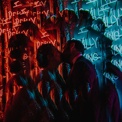 newly wed couple kissing front of neon lights using a kaleidoscope filter