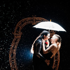newly wed couple stood in the dark in the rain under an umberella they are back lit so you can see all the rain droplets
