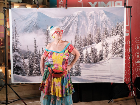  A costumed figure in bright colors stands before a printed snowy landscape backdrop. Viewable while standing or seated. High color saturation and contrast.