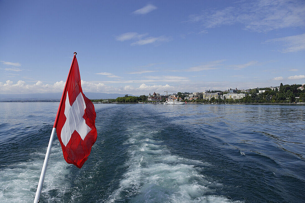 Swiss flag waves over lake with distant city view HOME Swiss Flat Rental