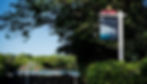 A sign for "The Anglers" pub by Fuller's, surrounded by trees. A blue sky and a suspension bridge are visible in the sunny background.