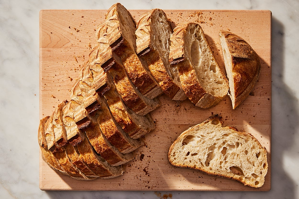 Sliced loaf of bread with a golden crust on a wooden cutting board, set on a marble surface. Crumbs are scattered around.