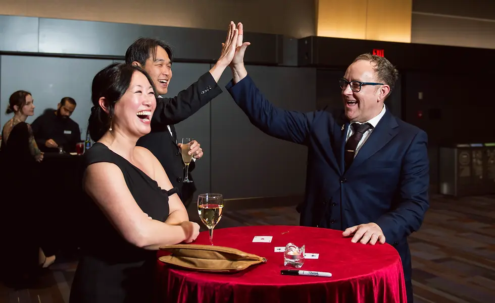 Vancouver corporate magician Bro Gilbert high fiving a laughing guest at a corporate event with playing cards on the table