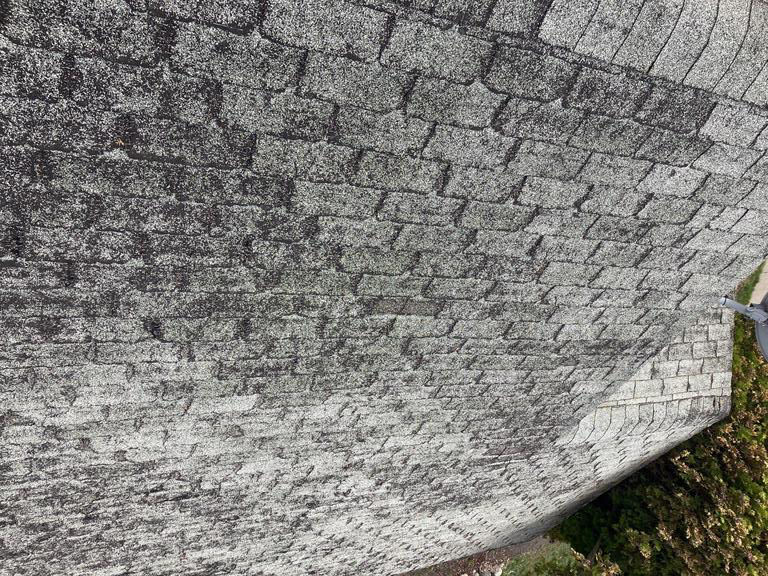 Close-up of a weathered gray shingle roof with dark patches.