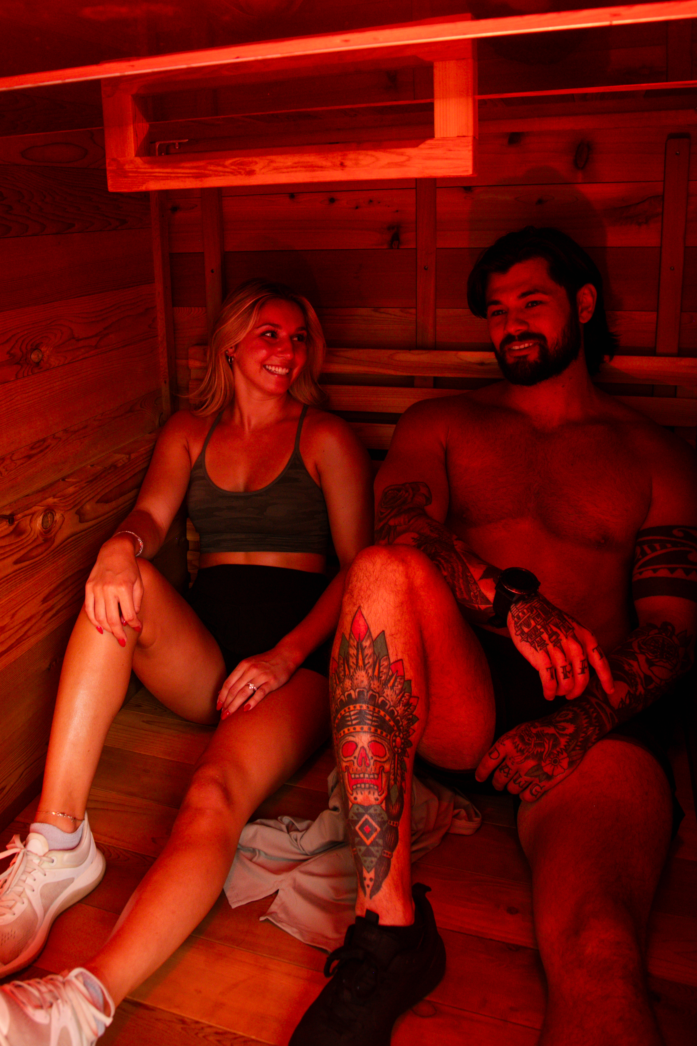 Two people sitting together on the bench inside The Hot Box Sauna XL under red light