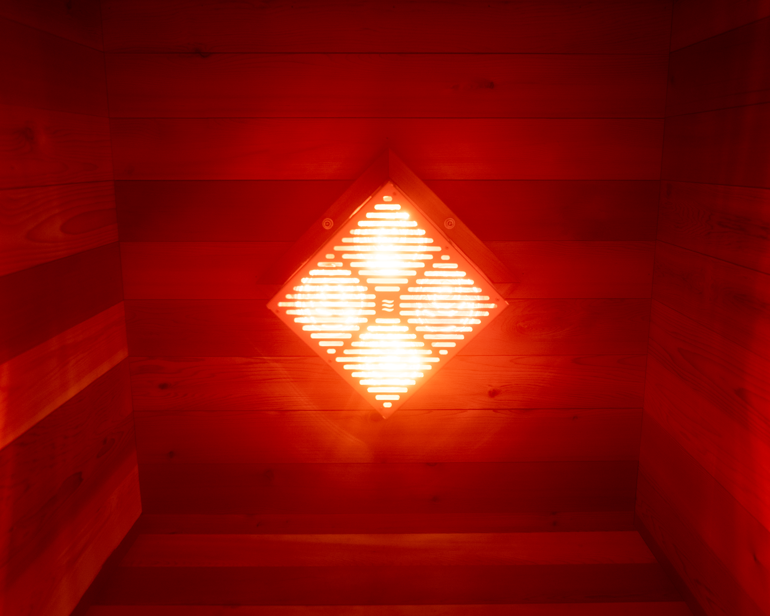 The diamond-shaped infrared and red light emitter glowing on the wall inside The Hot Box Sauna XL