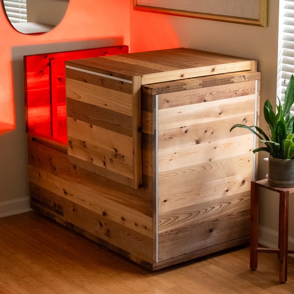 The Hot Box Sauna Standard in a room with a wood floor, lid raised and red light glowing inside the cabin