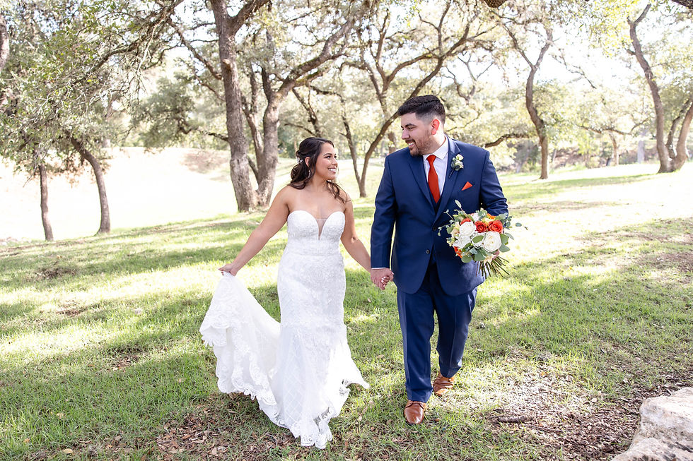 Bride in a white gown and groom in blue suit walk hand-in-hand through a sunny, wooded park. She carries her train, and he holds flowers. wedding venue near me, new braunfels wedding venue, Austin wedding venue, San Antonio wedding venue, hotel near me, hotel new braunfels, romantic restaurant near me, best proposal area in new Braunfels, best proposal area in Austin, wedding venue near Austin, destination wedding venue, wedding venue with onsite lodging, wedding venue Gruene TX, wedding venue New Braunfels TX, Hill Country wedding venue, Central Texas wedding venue, wedding venues near Austin TX, wedding venues near San Antonio TX, destination weddings Texas Hill Country, rustic wedding venue New Braunfels, Gruene event space, wedding venue with onsite lodging Texas, wedding venue with accommodations Gruene, stay and play wedding venue, wedding venue with guest lodging, Texas wedding venue with cabins, indoor and outdoor ceremony space, scenic wedding venue in Texas, wedding venue with included décor, decorated wedding venue Texas, wedding venue with landscaping, garden wedding venue Central Texas, picturesque wedding venue near Austin, nature-inspired wedding venue, best wedding venue in Gruene with lodging, where to get married in New Braunfels, romantic Hill Country wedding venue, wedding venue with bridal suite and lodging, beautiful outdoor wedding venue in Texas, elegant indoor reception space near Austin, unique Texas wedding venue with natural beauty, ceremony and reception in one location.