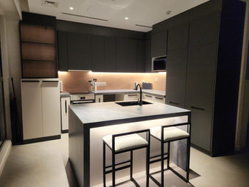 Completed modern kitchen with ambient and under-cabinet lighting, dark cabinetry, and a central island with seating.