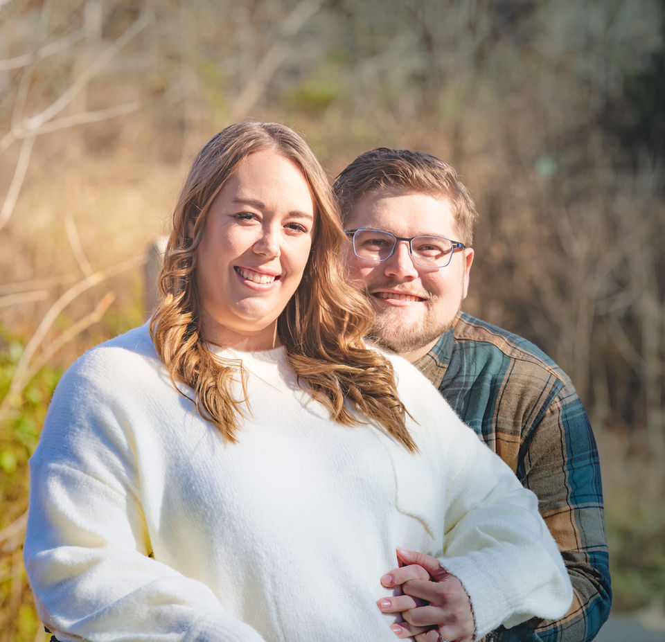 Couple outside in field embrace looking at camera.