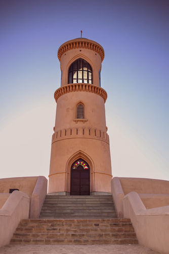 Hoge toren met trap en deuren, Dutchie in Oman, tegen blauwe lucht.