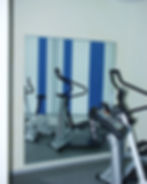 Ein großer Wandspiegel in einem Fitnessraum spiegelt Heimtrainer und blau-weiße Vorhänge wider.
