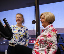 Kim happily turns the exercise bike on for a smiling female patient.