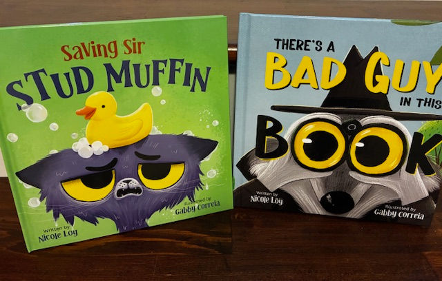 Two childrenās books on a wooden table: Saving Sir Stud Muffin with a duck on a grumpy cat, and Thereās a Bad Guy in This Book.