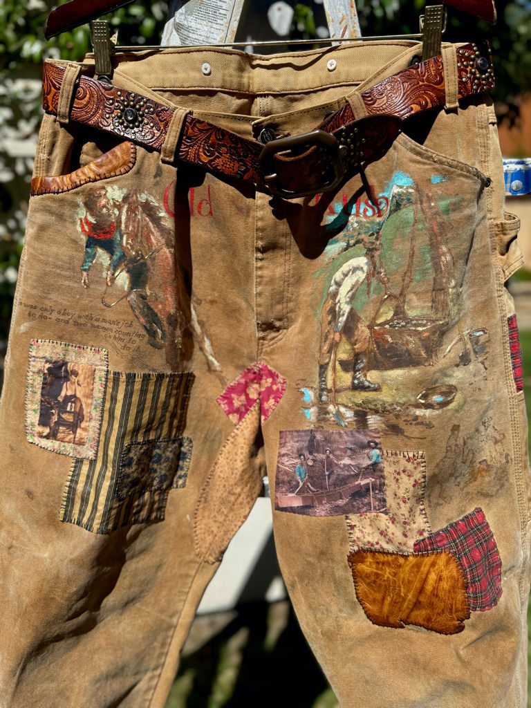 Thumbnail: Full front composition of “The Outlaw” work pants with hand-painted figures and layered patchwork elements