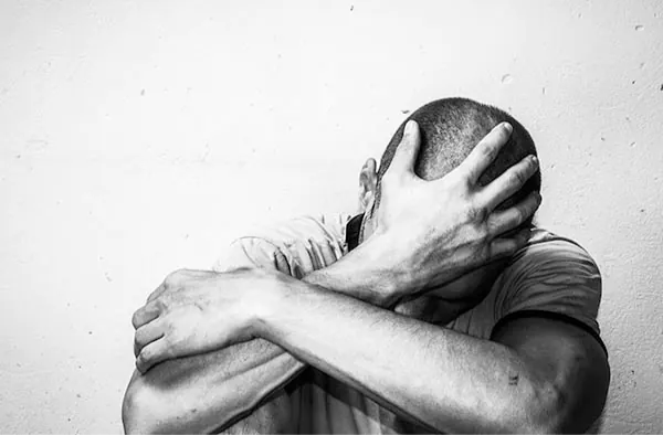 A man looking down while holding his head appearing to be struggling with something. 
