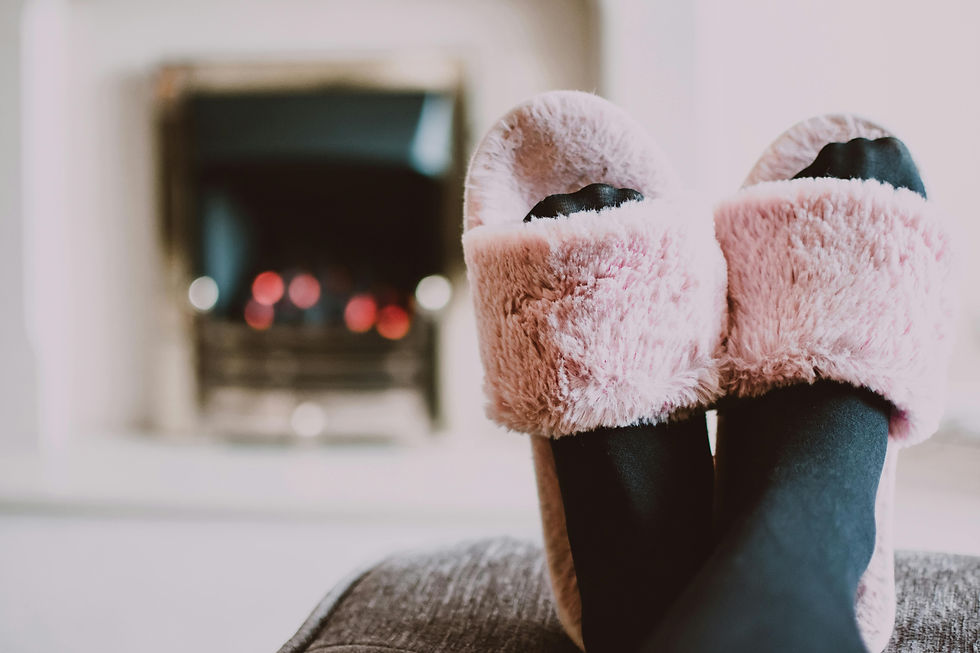 Fuzzy pink slippers on feet, relaxed near a cozy fireplace. Soft lighting and warm ambiance suggest comfort and relaxation.