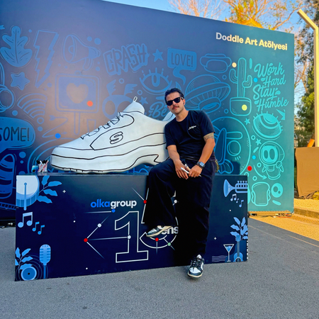 Event attendees holding brushes and markers, painting color onto the giant 3D shoe sculpture at the OLKA anniversary celebration.