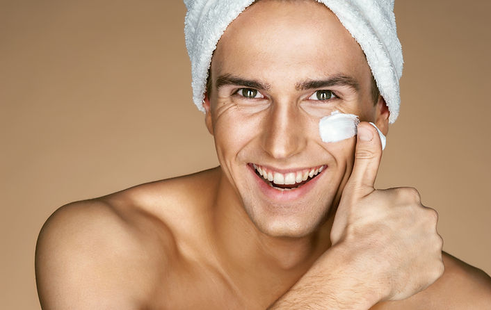 Young man with moisturizer on the face. Photo of smiling man on beige background. Grooming