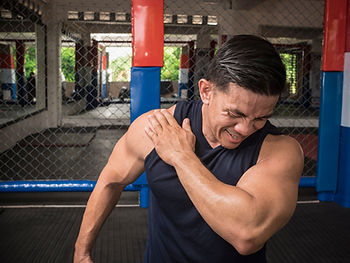 Man in workout clothing holding his shoulder in a gym.