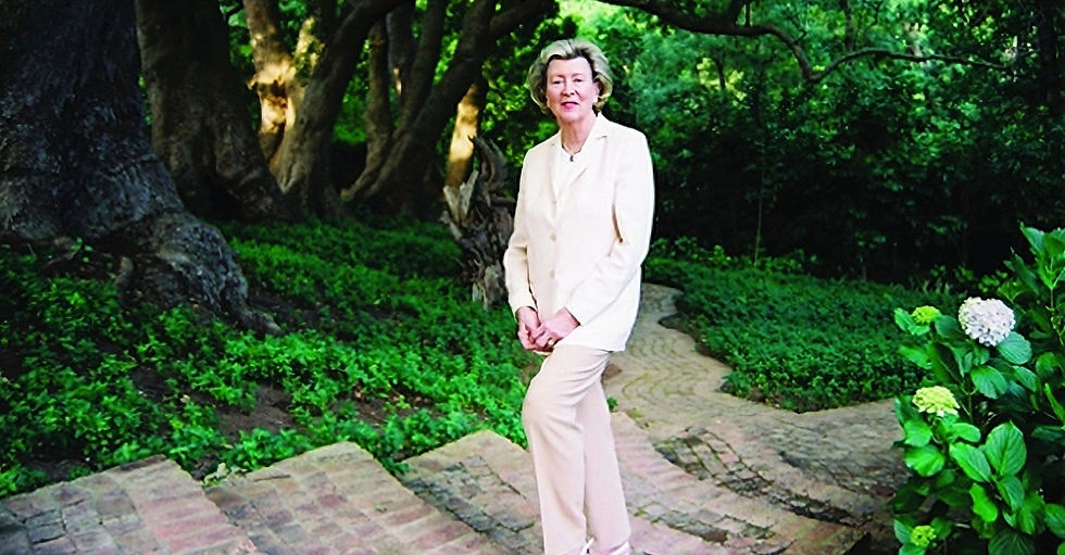 Elegant woman in a cream suit stands on a brick path in a lush garden with trees and hydrangeas, exuding a calm, serene mood.