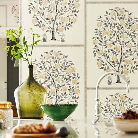 Kitchen countertop with black and yellow fruit tree wallpaper, a green bowl, glass vase with greenery, and a silver faucet