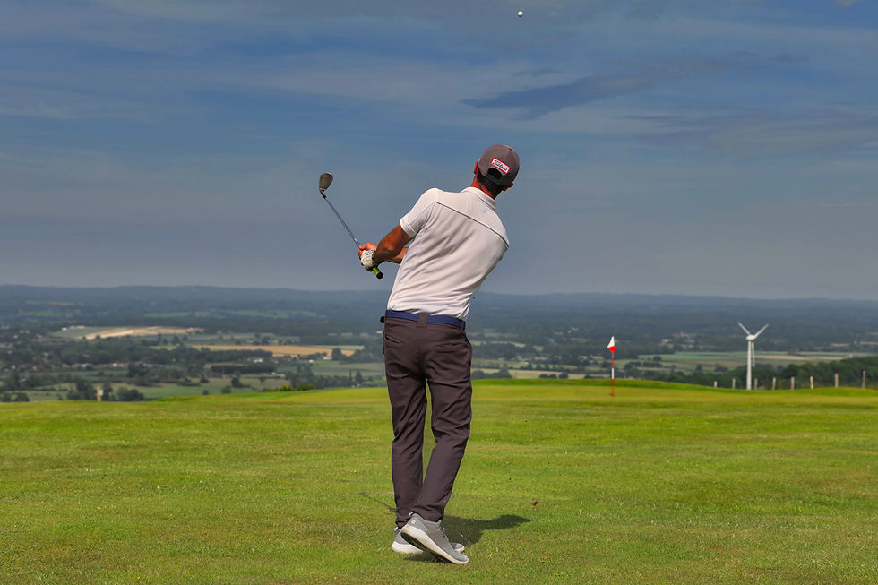 A golfer chips a shot towards the 7th green at lewes Golf Club with the wind turbine at Glynde in the distance.